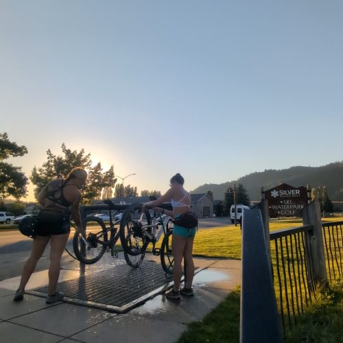 Two women using a bike washing station after riding their mountain bikes.